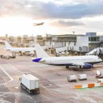 Airplanes at airport gates during sunset with ground vehicles and jet bridges