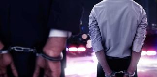 Two men in handcuffs with police lights in the background