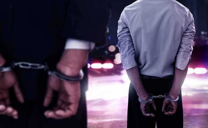shutterstock_1038568315 Two men in handcuffs with police lights in the background