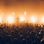 Rock band performing on stage with bright backlights and cheering crowd