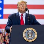 person speaking at a podium with U.S. flag backdrop