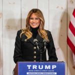 Melania’s Quiet Dealings Rattle Moscow woman speaking at podium with microphones and US flags