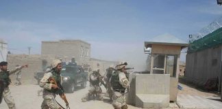 Soldiers in desert uniforms run past a checkpoint amid dust