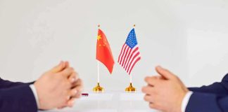 Two diplomats sit across table with China and United States flags between them