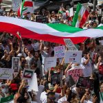 Iran’s Chilling ‘Retribution’ Stuns Rights Groups Crowd of protesters holding signs and a large tricolor flag