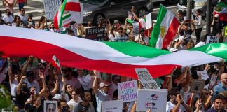 Iran’s Chilling ‘Retribution’ Stuns Rights Groups Crowd of protesters holding signs and a large tricolor flag