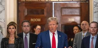 Tense Moment: Trump Walks Off For Grieving Parents Man in blue suit speaking to press indoors, flanked by several people
