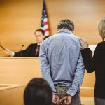 Trusted Recruiter Exploits Recruits — Bank Chaos Defendant in handcuffs stands before a judge in a courtroom