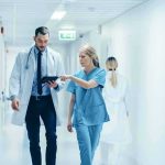 Landmark Hospital Settlement SHOCKER — $10 Million Fallout Doctor and nurse walking in a hospital corridor reviewing a tablet