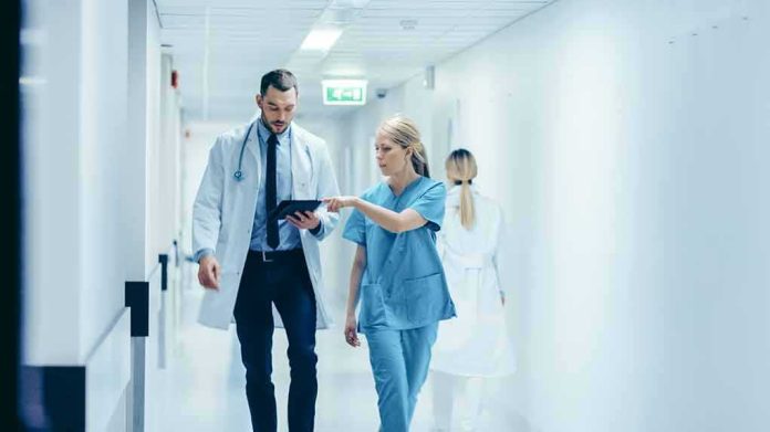 shutterstock_1189798168 Doctor and nurse walking in a hospital corridor reviewing a tablet