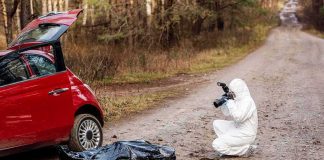 forensic investigator photographing evidence near red car on dirt road