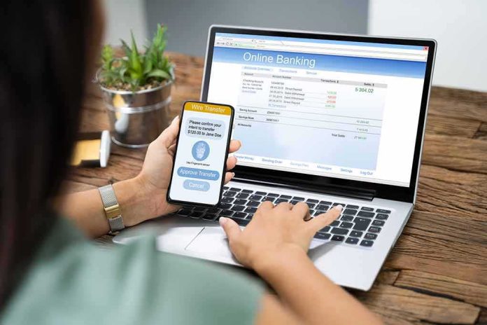 shutterstock_1542438851 Person using smartphone to approve bank transfer beside laptop with online banking