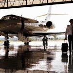 Pilot walking with suitcase beside private jet in hangar