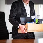New York Exodus: Who’s Cashing Out? Office worker in suit carrying a box of personal items