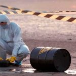 Bomb Squad Swarms US-Linked UK Base Hazmat worker kneeling near a fallen barrel at a cordoned-off site