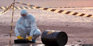 Bomb Squad Swarms US-Linked UK Base Hazmat worker kneeling near a fallen barrel at a cordoned-off site