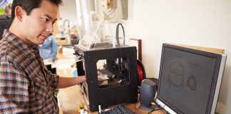 Man operating a 3D printer next to a computer with CAD designs