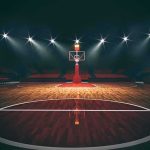 Basketball hoop on an empty indoor court under bright arena lights