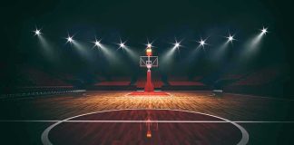 Basketball hoop on an empty indoor court under bright arena lights