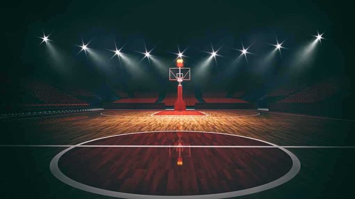 shutterstock_1933345100 Basketball hoop on an empty indoor court under bright arena lights