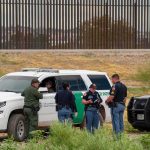 Supreme Court Greenlights Border Turnbacks law enforcement officers confer beside patrol vehicles near a border fence