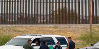 Federal Shooting, No Footage – Credibility Craters law enforcement officers confer beside patrol vehicles near a border fence