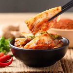 Chopsticks lifting kimchi from a black bowl