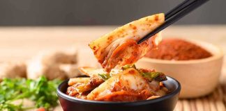 Chopsticks lifting kimchi from a black bowl