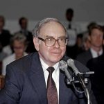 Older man in suit speaking at microphones during hearing