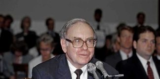 Older man in suit speaking at microphones during hearing