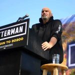 Fetterman’s GOP Cameo Shocks Democrats Speaker at outdoor rally standing at podium with microphone
