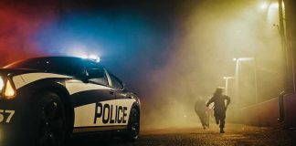 Crash, Tears, PRAYERS – Campaign In Flames? Police car with flashing lights at night as two people run in a foggy alley