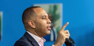 Man speaking at a microphone with raised finger