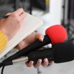 Boot Camp Outbreak Triggers Stunning Reversal Journalist holding two microphones while writing in a notebook