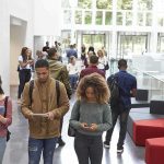 Mocked Murder Erupts At TPUSA Summit Students walking through a bright campus lobby using mobile devices