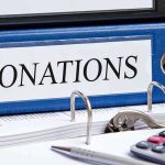 Blue binder labeled donations on a desk with papers and a calculator