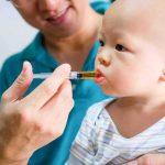 Baby taking liquid medicine from an oral syringe held by an adult