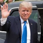 Donald Trump waves while standing beside a black vehicle