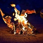 Hands burning cash over a small fire at night