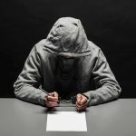 Bomb Plot Alleged – Chilling Attack Detailed Person in gray hoodie writing while handcuffed at a table