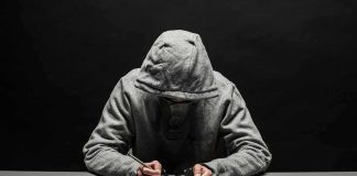 Bomb Plot Alleged – Chilling Attack Detailed Person in gray hoodie writing while handcuffed at a table