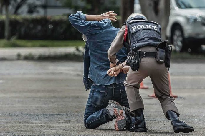 shutterstock_1345792937 Police officer handcuffing person kneeling on pavement