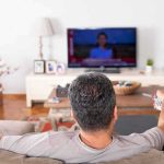 Man watching TV from couch with remote in hand