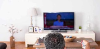 Football Night Ends In Felony? Man watching TV from couch with remote in hand