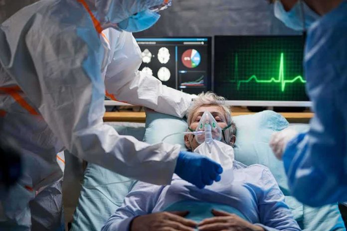 shutterstock_1661222104-1 Patient on hospital bed with oxygen mask and medical staff in protective gear