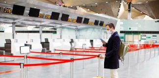 Cross-Border Ebola – Tracing Race Begins Traveler wearing a mask stands by yellow suitcase at empty airport check-in