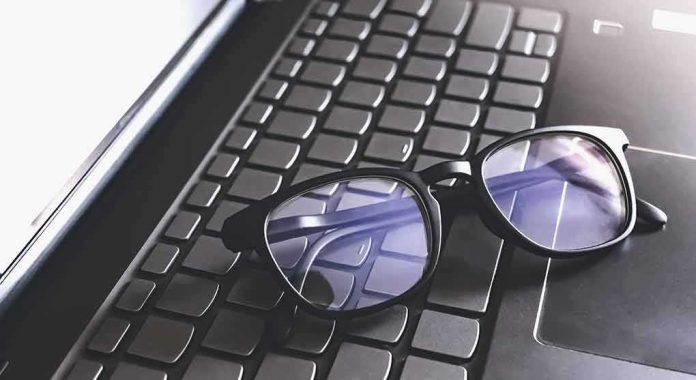Black eyeglasses resting on a laptop keyboard