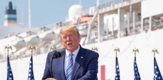 DOJ Blasts Hospital Gatekeepers Donald Trump speaking at a podium with American flags and a ship in the background